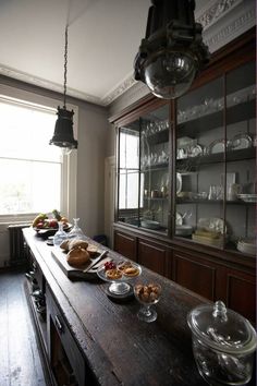 a long wooden table topped with plates and bowls filled with food next to a window