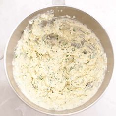 a metal bowl filled with food on top of a white countertop next to utensils