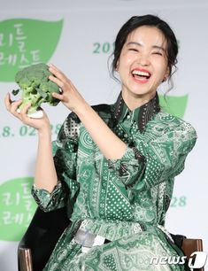 a woman holding up a piece of broccoli in front of her face and smiling