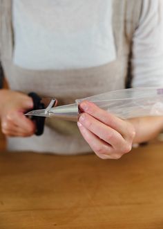 a woman holding a pair of scissors on top of a wooden table next to a plastic bag