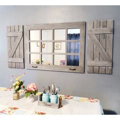 a dining room table with flowers and utensils in front of two windows on the wall