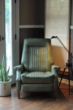 a green chair sitting in front of a window next to a potted plant