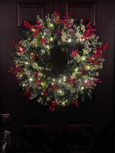 a christmas wreath with lights hanging from the front door, on a dark wooden door