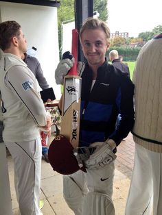 a man standing next to another man holding a cricket bat