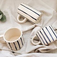 two coffee mugs sitting on top of a bed next to a vase with flowers