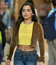 a woman wearing jeans and a crop top walking down the street with her hand in her pockets