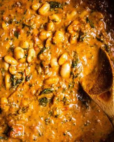 a wooden spoon in a pot filled with beans and spinach