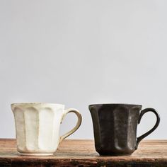 two black and white coffee cups sitting on top of a wooden table next to each other