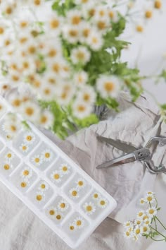 flowers and scissors are sitting on a table with white paper, daisies and green leaves