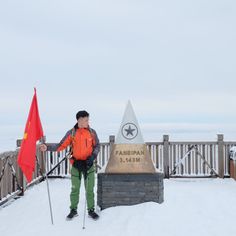 a man standing in the snow next to a flag and a monument with a star on it