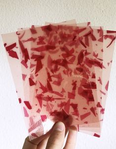 a hand is holding four pieces of red tissue paper in front of a white wall