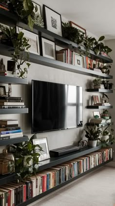 a living room with bookshelves, plants and a flat screen tv on the wall