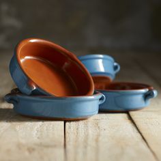 two blue dishes sitting on top of a wooden table next to each other with one bowl in the middle