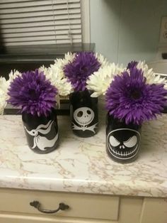 three black vases with purple and white flowers in them sitting on a counter top