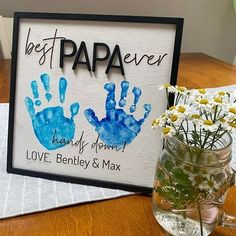 a vase filled with flowers next to a sign that says best papa ever and two handprints