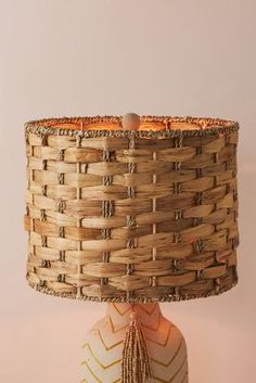 a woven lamp shade sitting on top of a wooden table next to a white wall