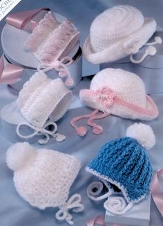 crocheted hats and mittens are displayed on a blue cloth with pink ribbons