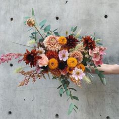 a person holding a bouquet of flowers in front of a concrete wall with holes in it