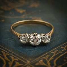 three stone diamond ring sitting on top of a blue velvet covered book with gold trimming