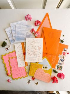 an assortment of wedding stationery and envelopes laid out on a white surface with rose petals