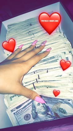 a woman's hand with pink fingernails and hearts on top of money in a box