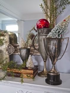 a mantle topped with silver cups filled with christmas decorations and greenery next to a mirror