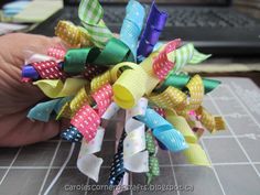 a hand holding a bunch of colorful hair bows on top of a table next to a laptop