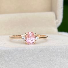 a pink diamond ring sitting on top of a white cloth covered box with its lid open