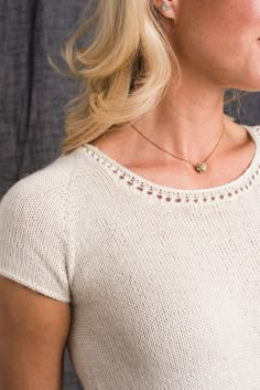 a blonde woman wearing a white sweater and gold necklace with a small diamond on it