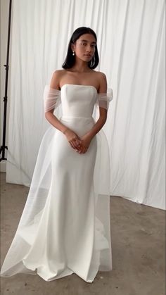 a woman standing in front of a white backdrop wearing a dress with sheer sleeves and an off the shoulder neckline