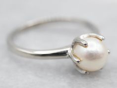 "This traditional pearl ring is as versatile as can be. Crafted of white gold, six prongs rise from the center, creating a perfect cup of gold for this classic centerpiece. A shining white pearl with a velvety iridescent luster, simply stunning!  Metal: 10K White Gold Gem: Pearl Gem Measurements: 5.9 mm, Round Ring Size: 5.75 Marks: \"10K DC\" Stamped on the inside band  To view a video of this piece check out the link below: https://vimeo.com/842621964 SKU #: A28908 Each piece has been identifi Ring Pearl, Silver Gift Wrap, Pocket Watch Chain, June Birthstone, Watch Chain, Round Rings, Simple White, Silver Gifts, June Birth Stone