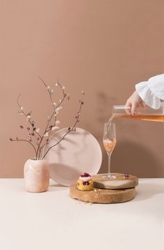 a person pouring wine into a glass on top of a wooden tray next to a plate