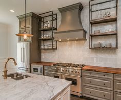 a kitchen with stainless steel appliances and marble counter tops, open shelving above the stove