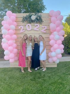 three women standing in front of a wooden sign with balloons