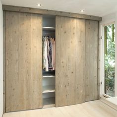 an open closet with clothes on hangers and sliding doors in front of a window