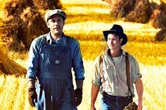 two men in overalls and hats walking through a field