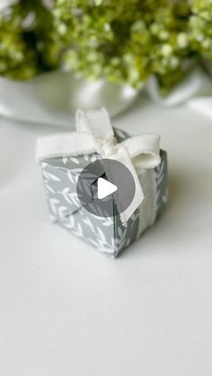 an origami box with a bow on it and flowers in the back ground