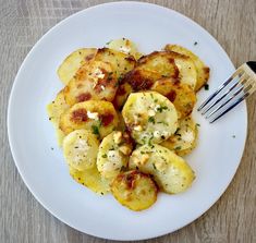 a white plate topped with potatoes covered in cheese and seasoning next to a fork