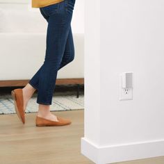 a woman in brown shoes walking past a white wall with a light switch on it