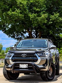 the front end of a silver toyota pickup truck parked in front of a large tree