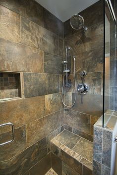 a walk in shower sitting next to a tiled wall and floor covered in brown tiles