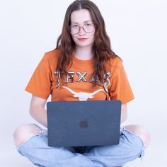 a woman sitting on the floor with a laptop in her lap and wearing an orange texas t - shirt