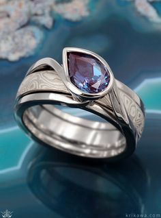 a ring with a purple stone in it on a blue surface and flowers behind it