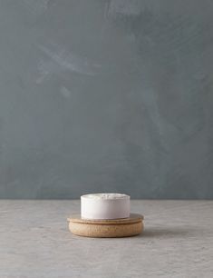 a small white cake sitting on top of a wooden coaster next to a gray wall