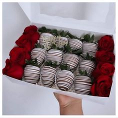 a box filled with chocolate covered strawberries next to red roses and two hands holding one