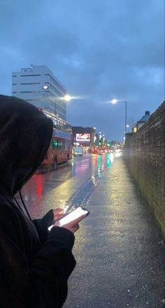 a person standing in the rain holding a cell phone and looking at something on their hand