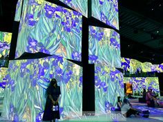 a woman is standing in front of an art exhibit with blue flowers on the walls