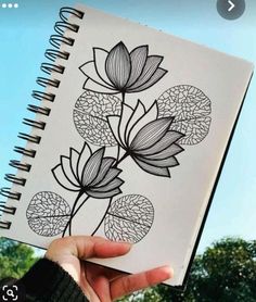 a person holding up a notebook with drawings on the pages and flowers drawn on it