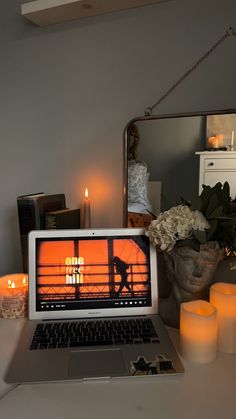 an open laptop computer sitting on top of a white desk next to candles and flowers