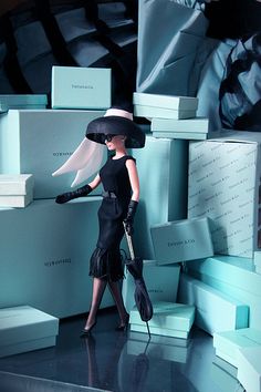 a woman in a black dress and hat standing next to stacks of boxes